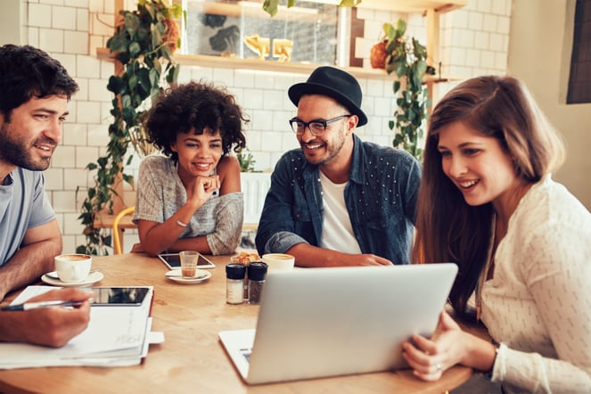 four people sit around a table looking at a laptop with Donorfy charity CRM on the screen
