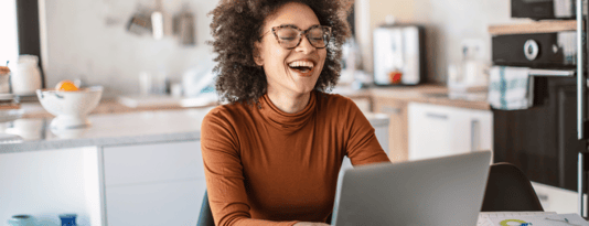 Women smiles and works on her laptop from her kitchen