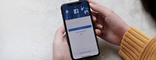 Woman holds phone in both hands with a Facebook login page on the screen