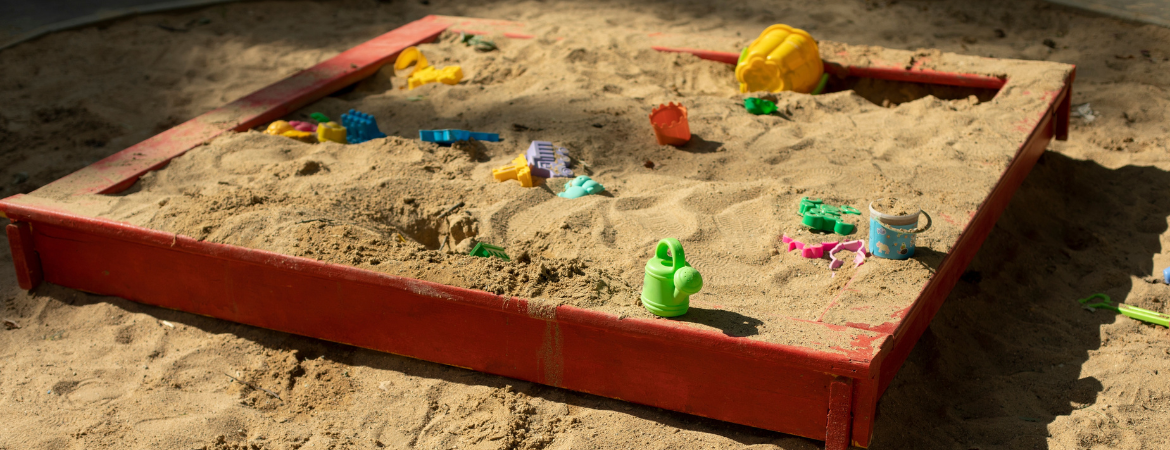 A large, square children's sandbox filled with colourful plastic toys